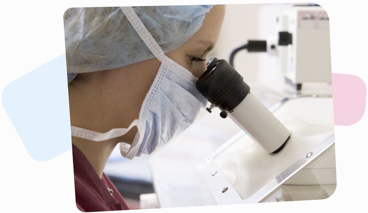 female doctor in a mask and a hospital bag on her hair looking through a microscope