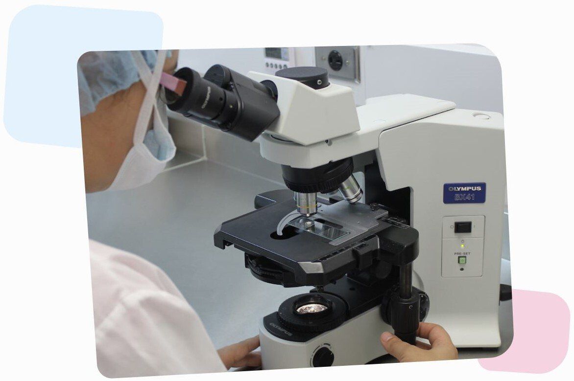 scientist wearing a hospital mask and glasses, looking through an Olympus microscope on an egg cell