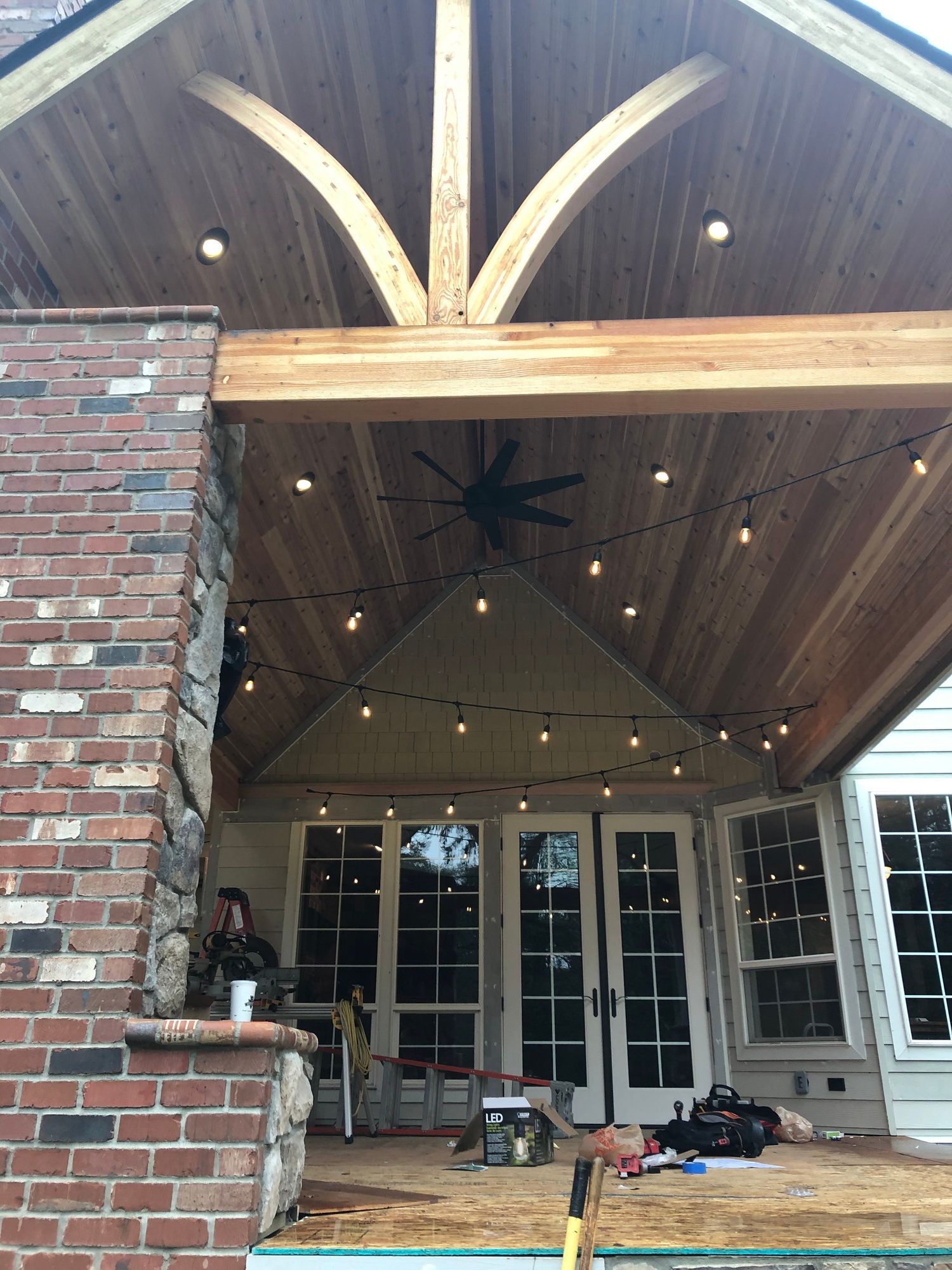 A porch with a wooden ceiling and a ceiling fan.