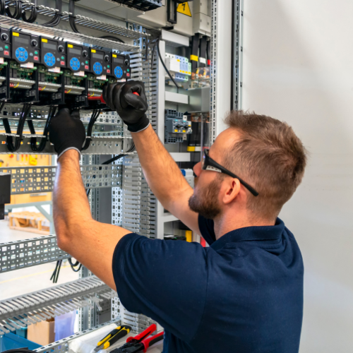 A man wearing glasses and gloves is working on an electrical box.