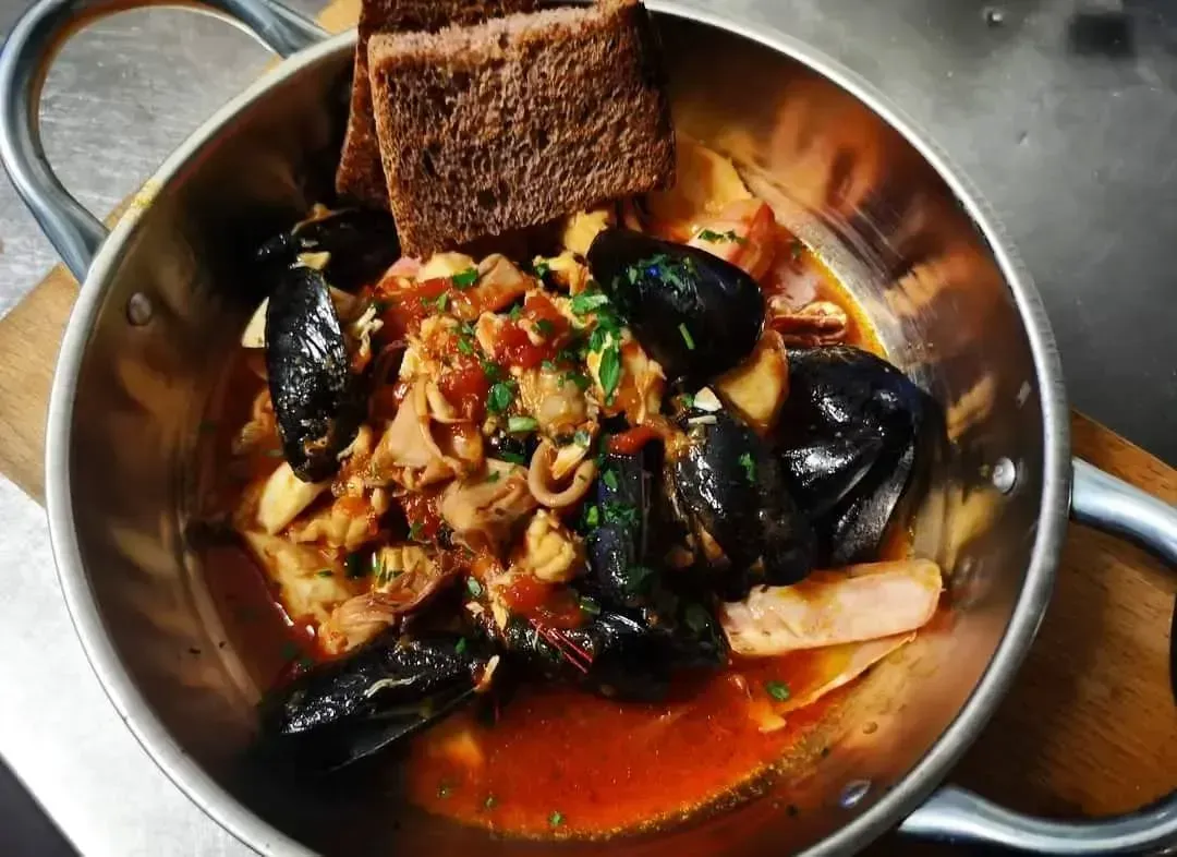 Pasta ai frutti di mare con gamberi, cozze, vongole e pomodori, guarnita con prezzemolo su un piatto bianco.