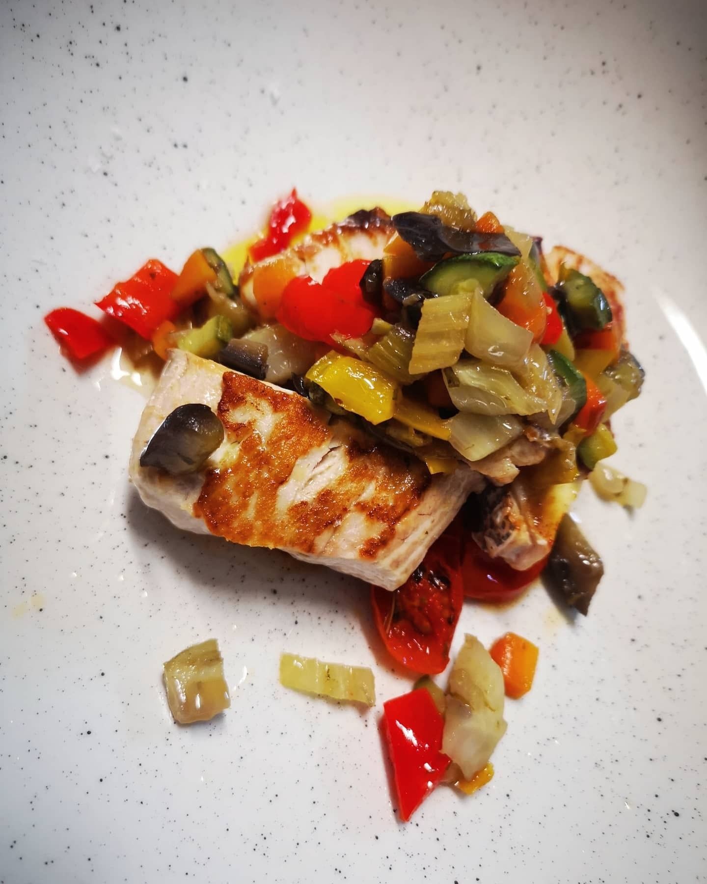 Un bicchiere di vino e una bottiglia su un tavolo. Il bicchiere è pieno di vino rosso. L'etichetta della bottiglia raffigura dei fiori blu.