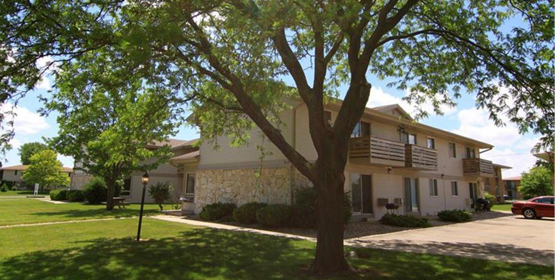 An exterior view of Tudor Oaks Apartments with large Oak tree and grass outside