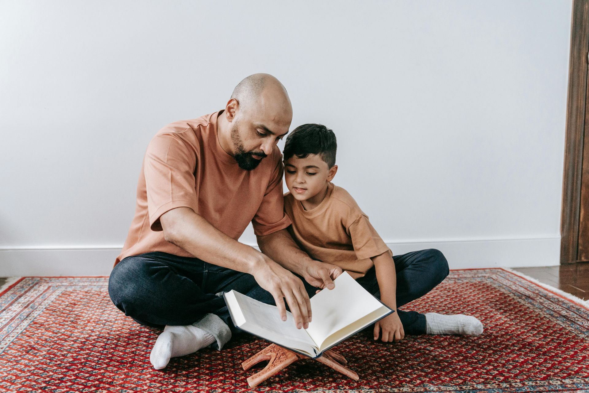A man and a boy are sitting on the floor reading a book.