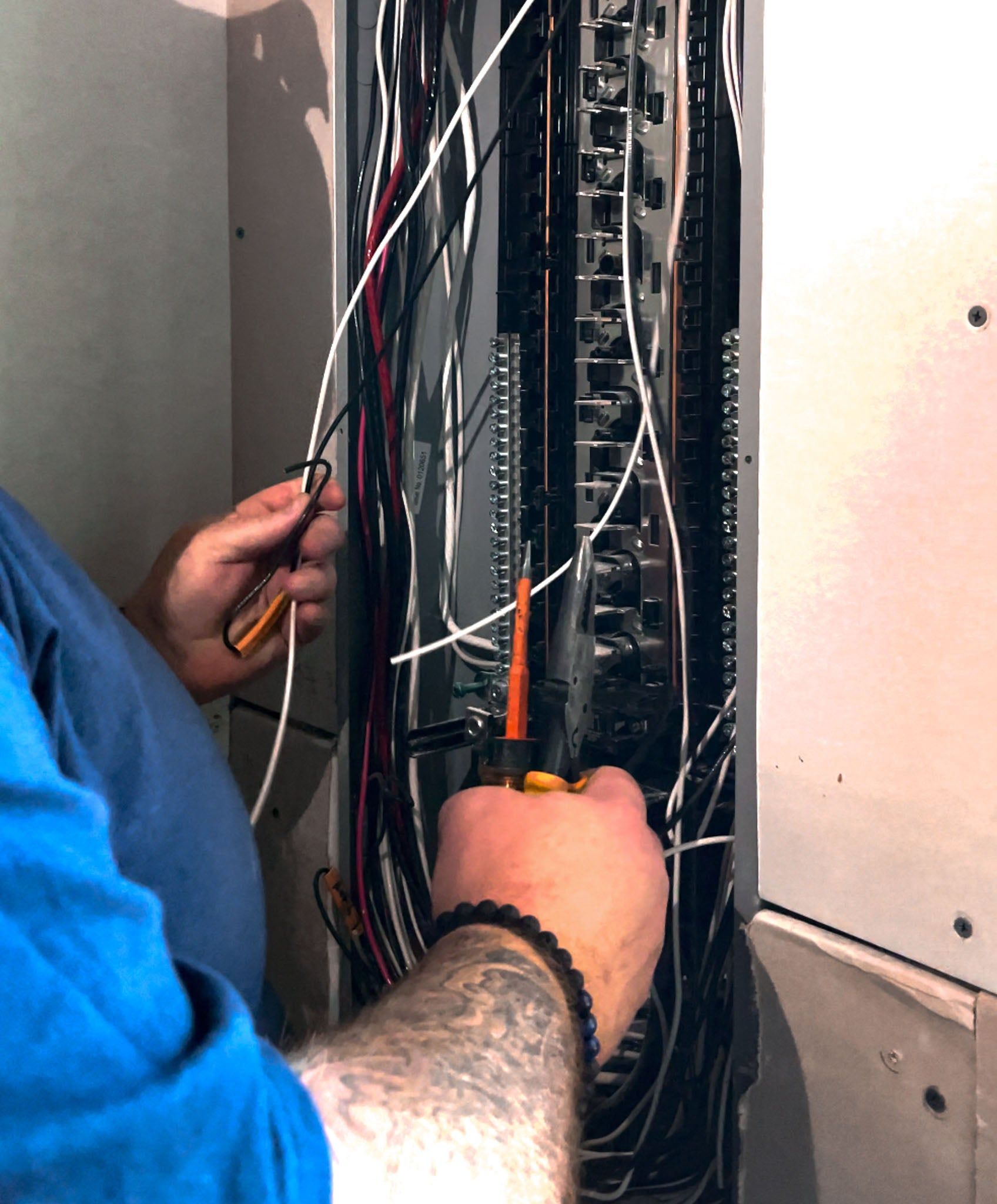 Technician wiring an electrical panel with pliers and cables inside a metal cabinet