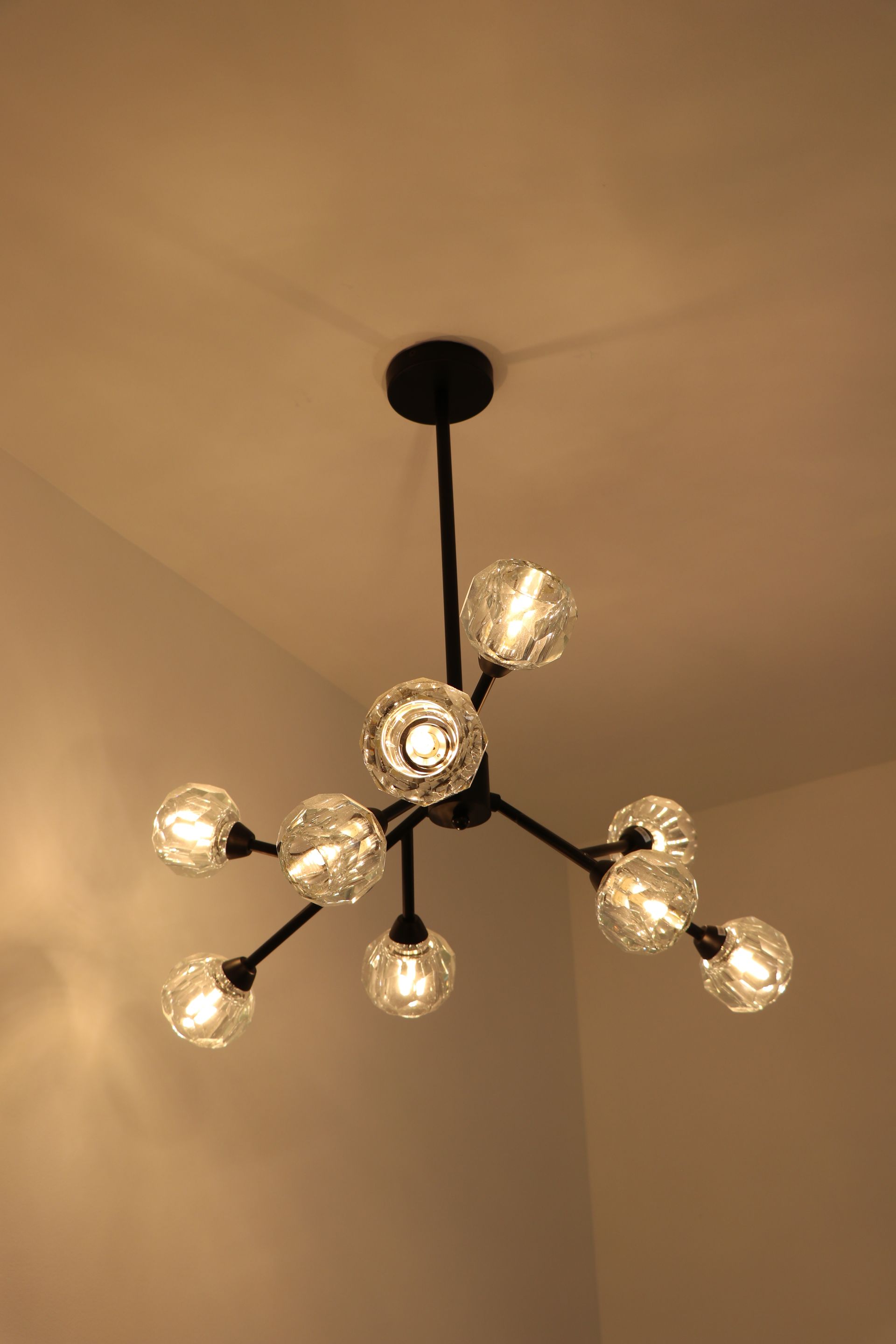 Crystal chandelier hanging from a ceiling in a gray stairwell, sparkling with bright lights.