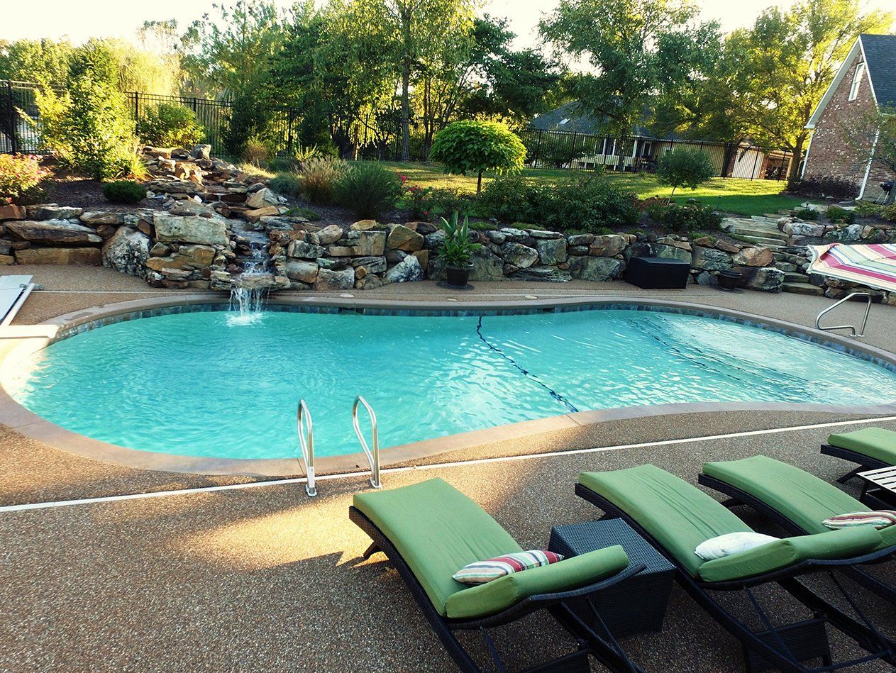 A large swimming pool surrounded by green chairs and a waterfall.