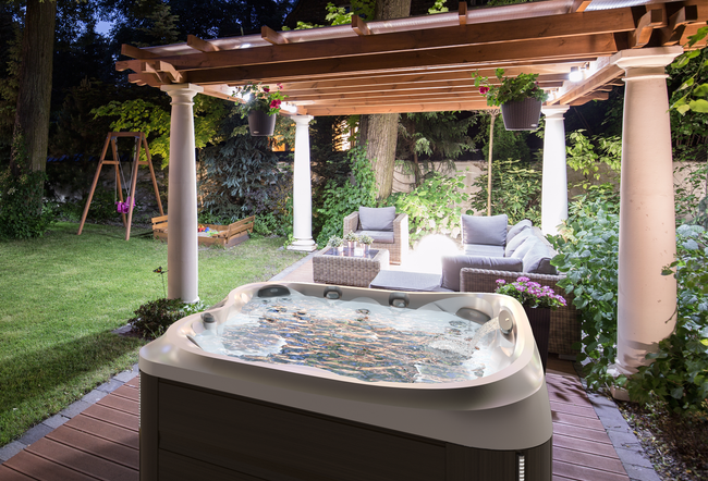 A hot tub is sitting under a pergola in a backyard.