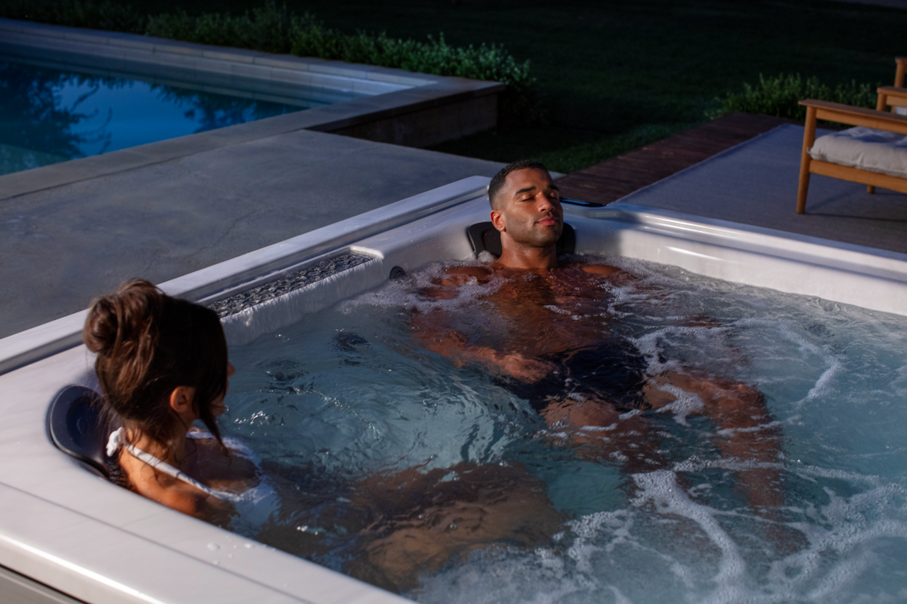 A hot tub is sitting under a pergola in a backyard.
