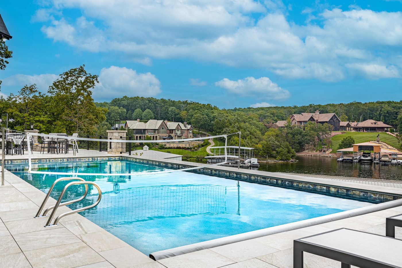 Swimming pool next to a lake with houses in the background under a blue sky.