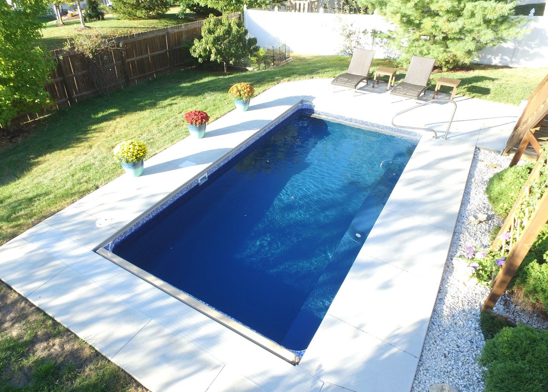 A large swimming pool in a backyard with chairs and flowers