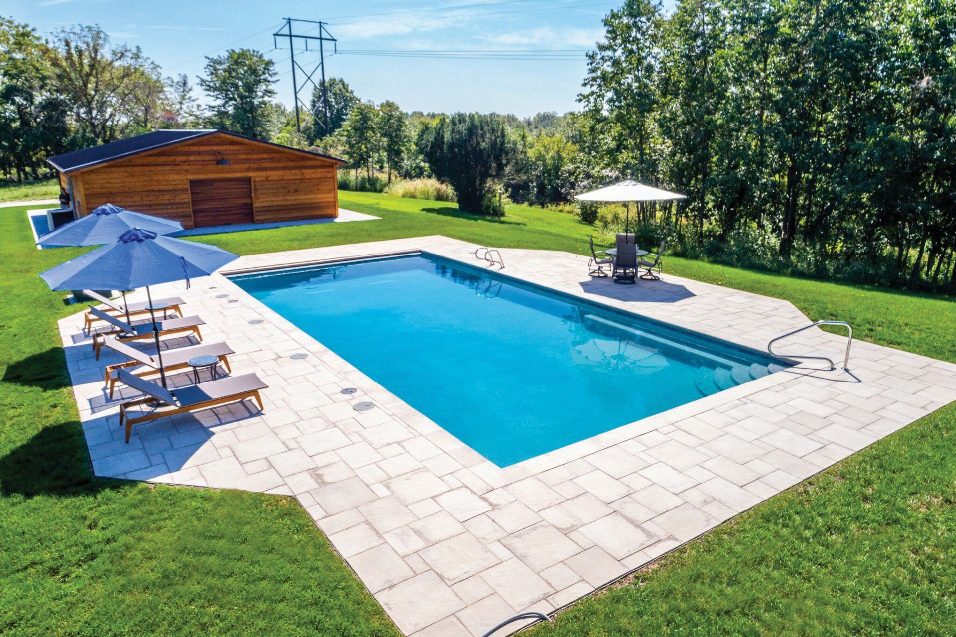 A large swimming pool surrounded by chairs and umbrellas in a lush green yard.