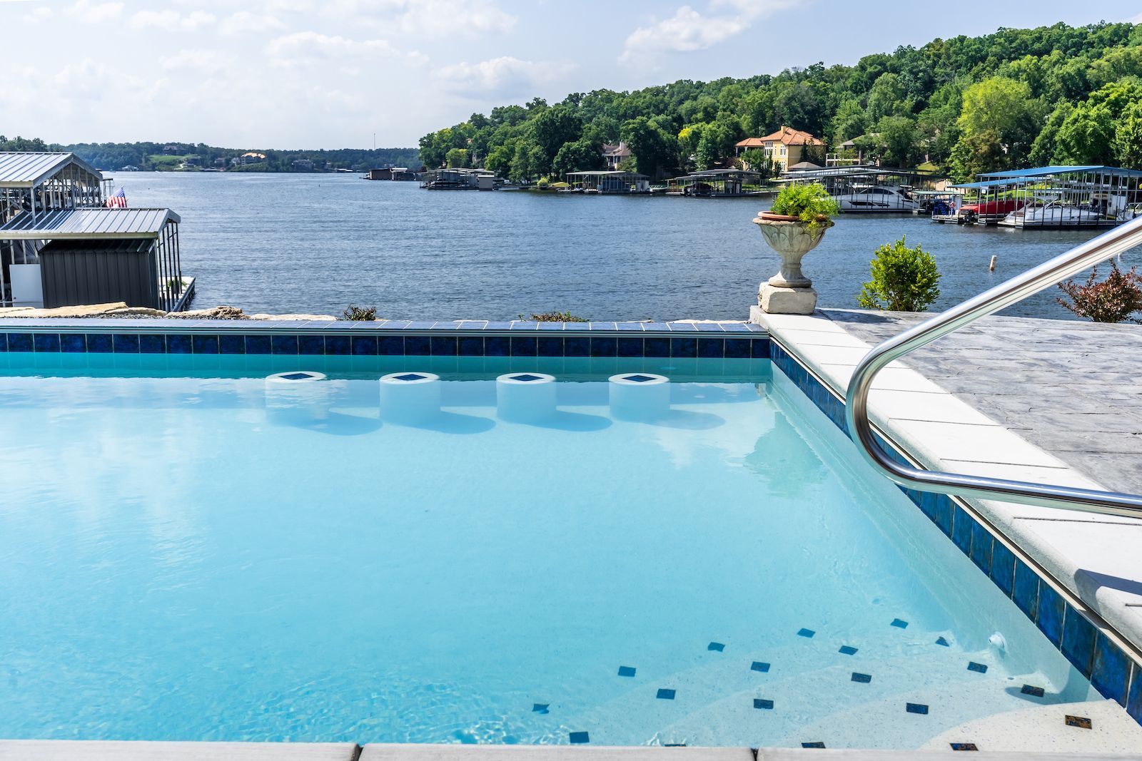 Swimming pool overlooking a lake with docks, trees, and sky; blue water, sunny day.