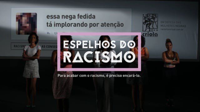 Um grupo de mulheres em frente a uma placa que diz espelhos do racismo