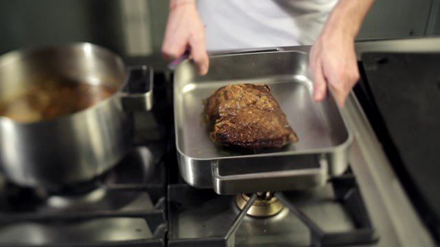Uma pessoa está colocando um pedaço de carne em uma panela no fogão.