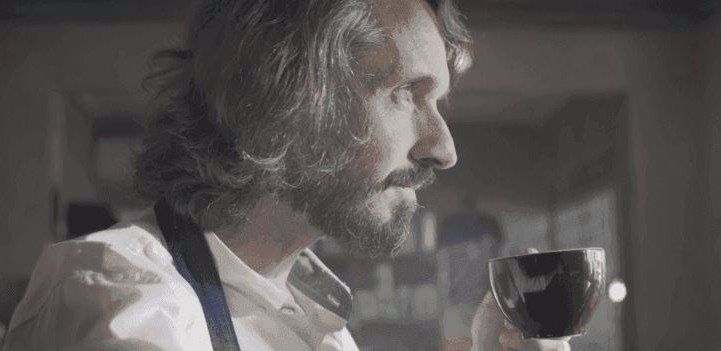 Um homem com barba está bebendo uma xícara de café.