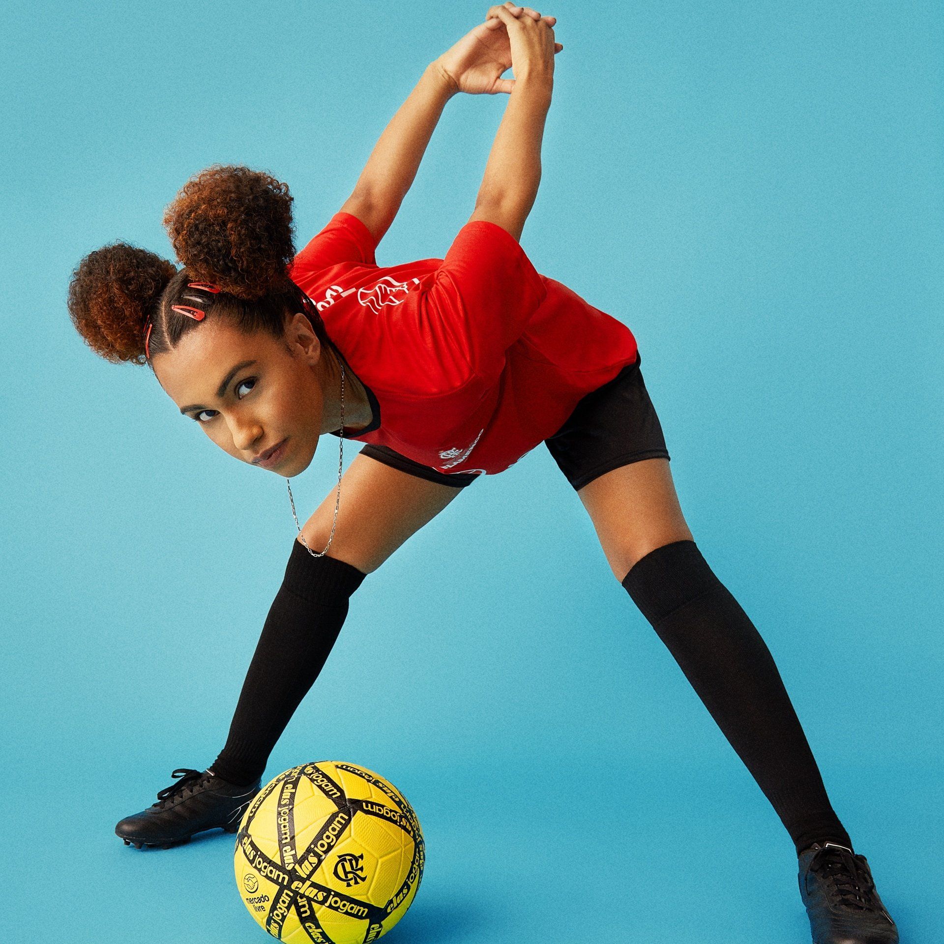 Uma mulher de camisa vermelha está se espreguiçando ao lado de uma bola de futebol amarela
