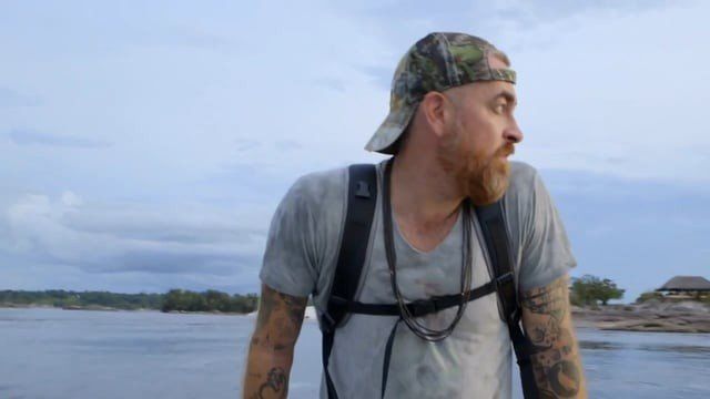 Um homem com uma mochila está parado ao lado de um corpo d'água.