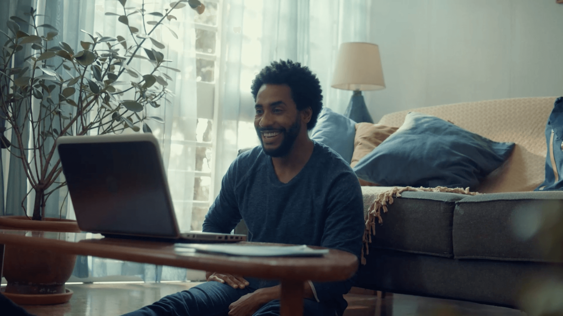 Um homem está sentado no chão em frente a um laptop.