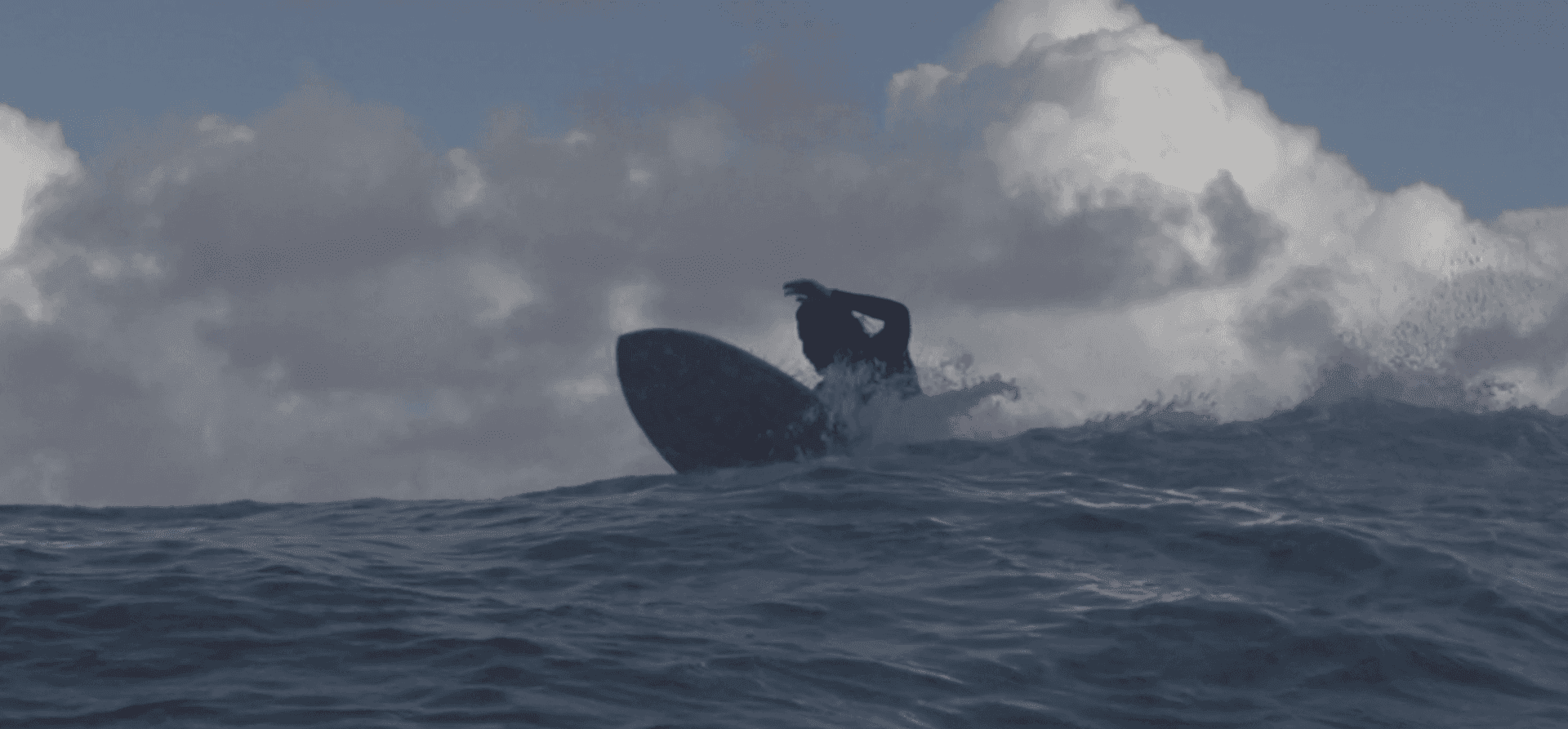 Um homem está surfando uma onda em uma prancha de surf no oceano.