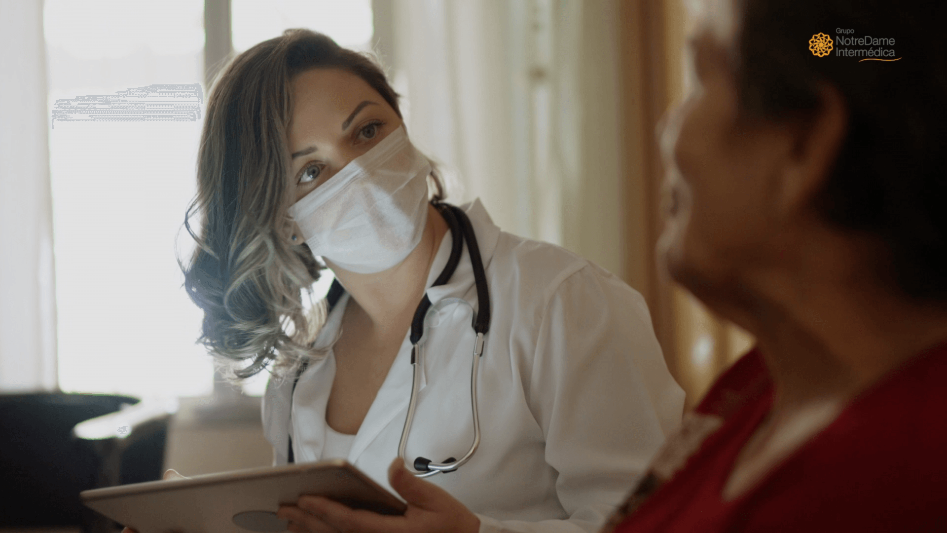 Um médico usando uma máscara está conversando com uma senhora idosa enquanto segura um tablet.
