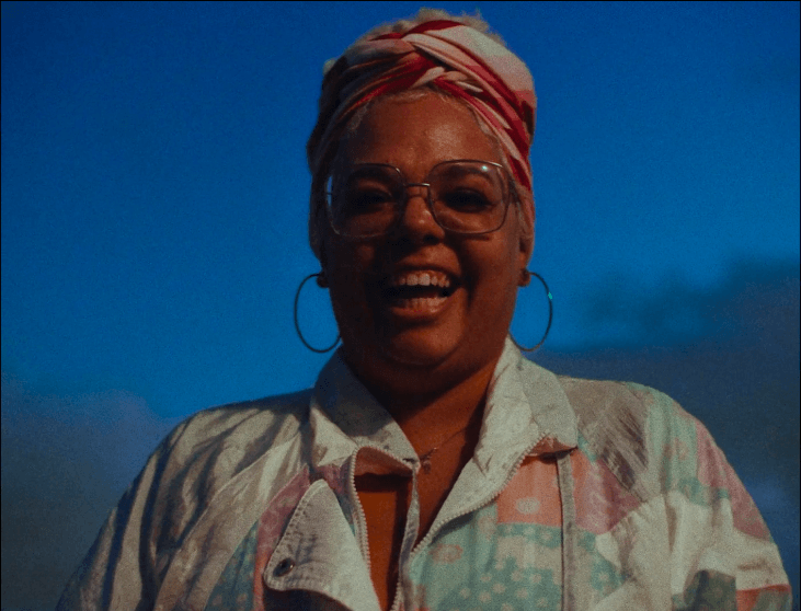 Uma mulher de óculos e lenço na cabeça está sorrindo.