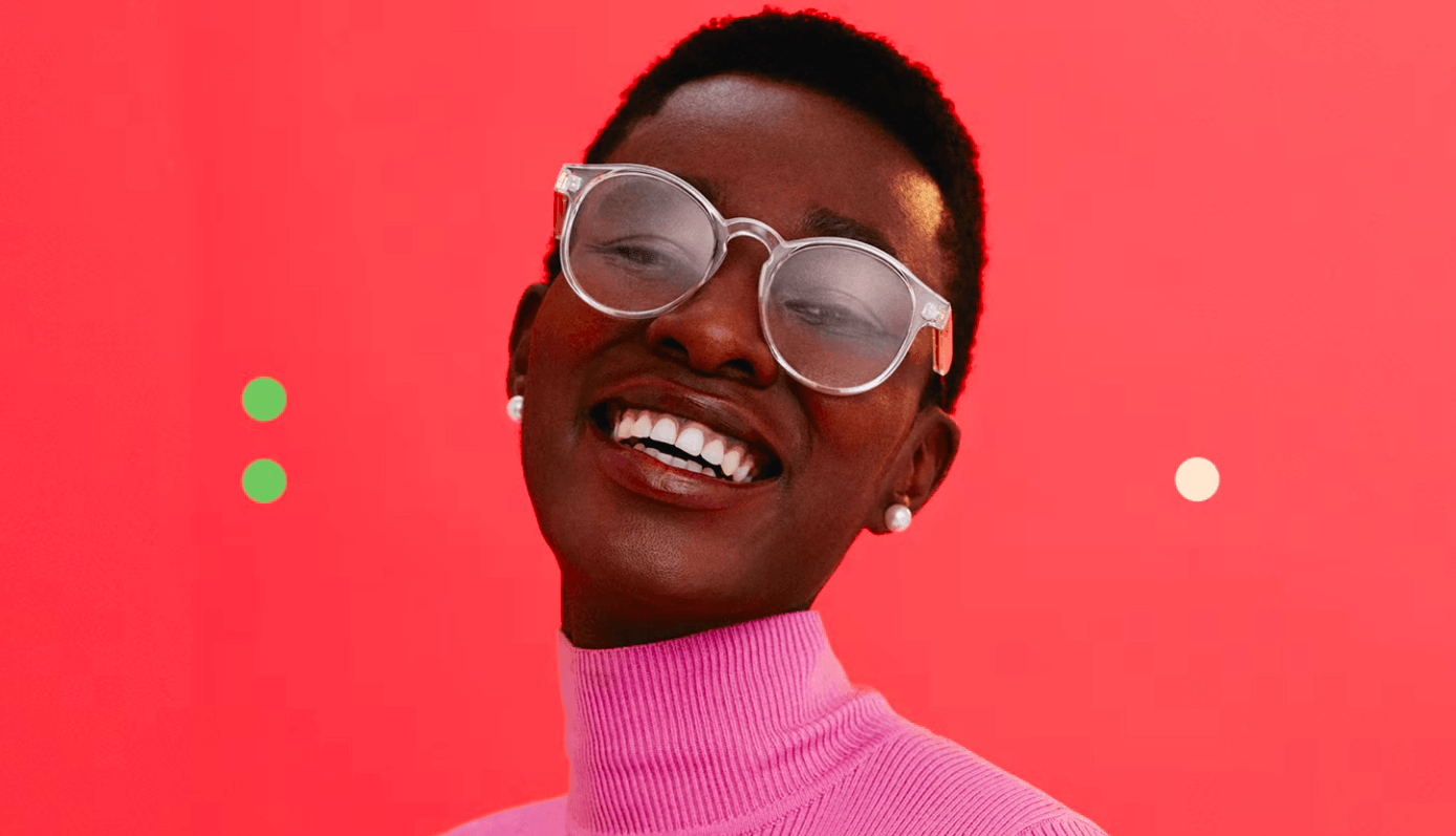 Uma mulher de óculos e um suéter rosa está sorrindo.