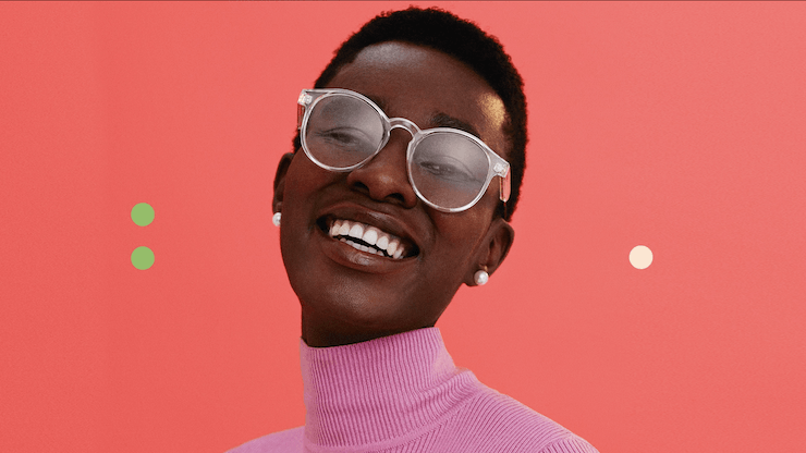 Uma mulher de óculos e um suéter rosa está sorrindo.