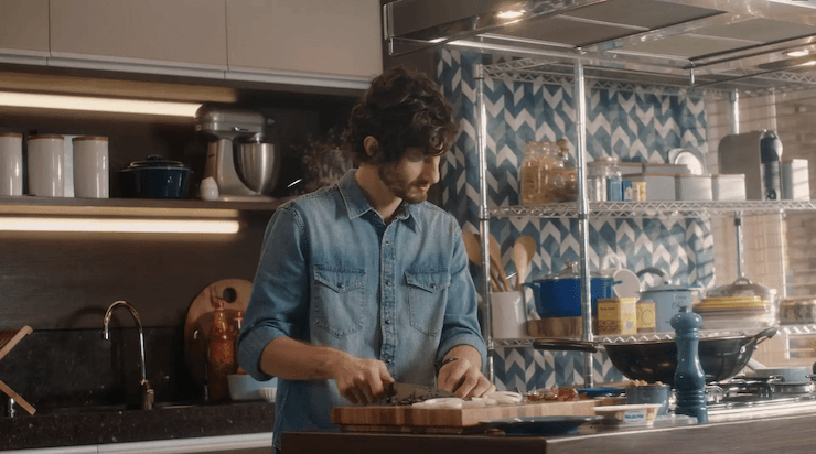 Um homem está cortando carne em uma tábua em uma cozinha.