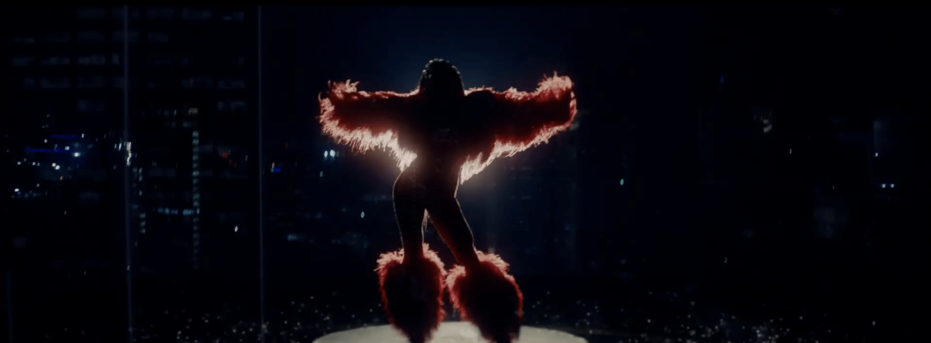 Uma pessoa está em um palco com os braços estendidos no escuro.