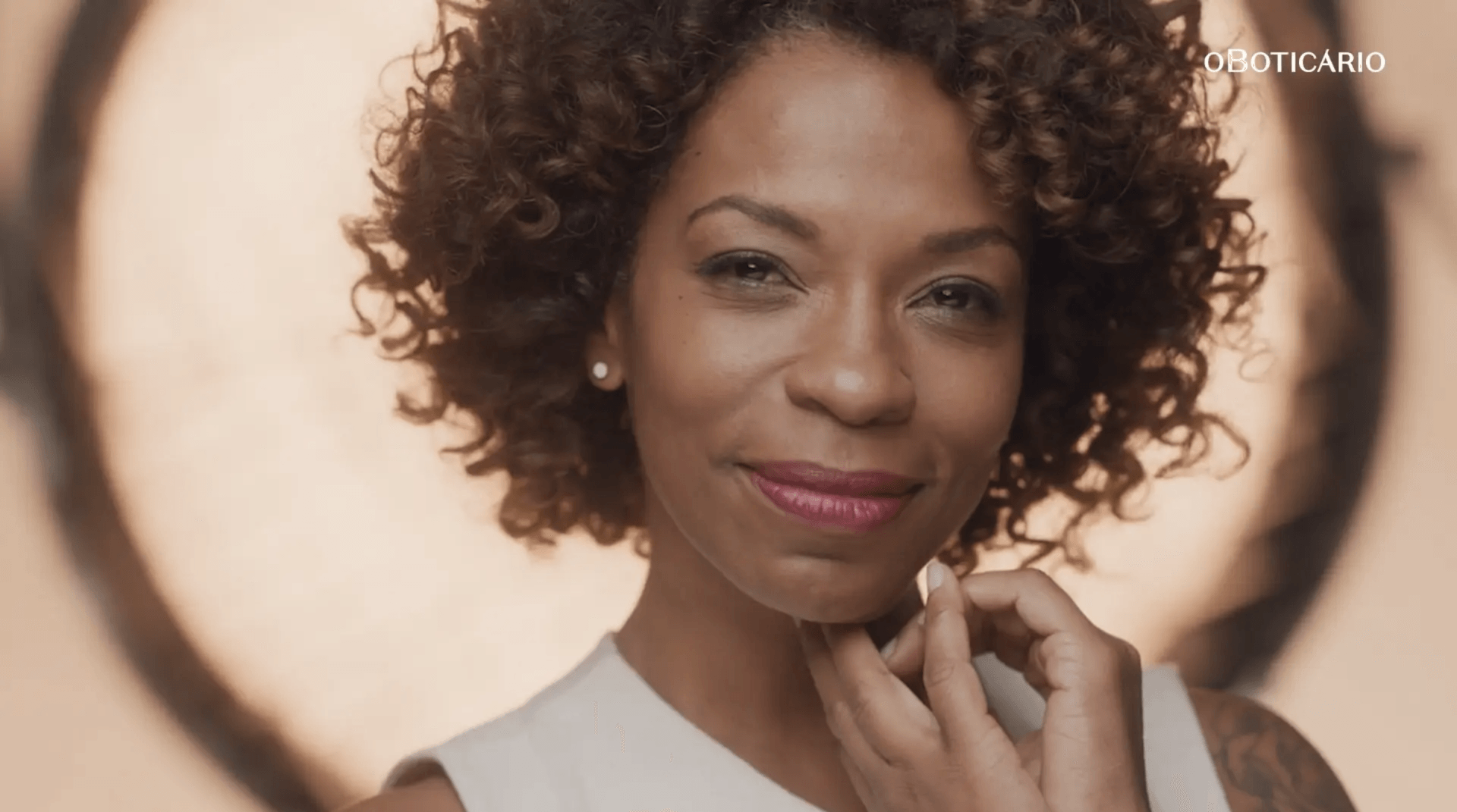 Uma mulher com cabelos cacheados está sorrindo e tocando seu rosto.
