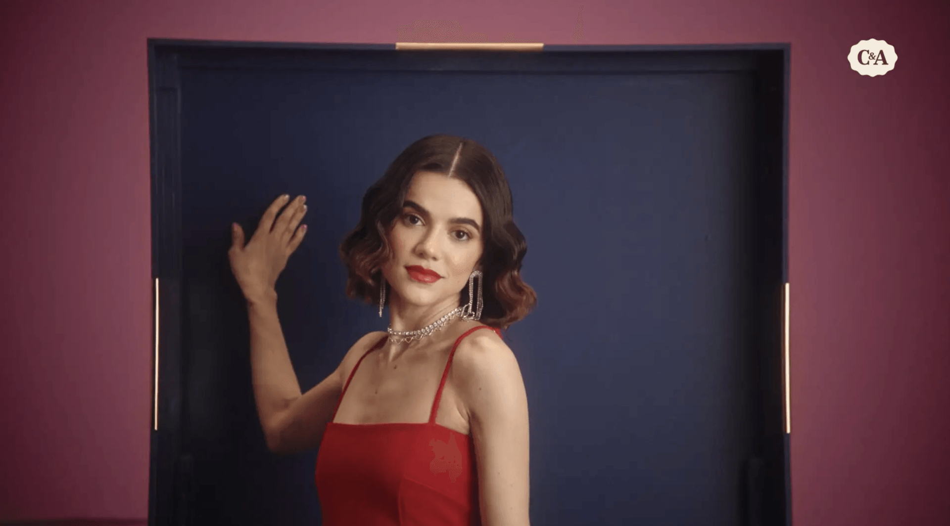 Uma mulher de vestido vermelho está parada em frente a uma porta.