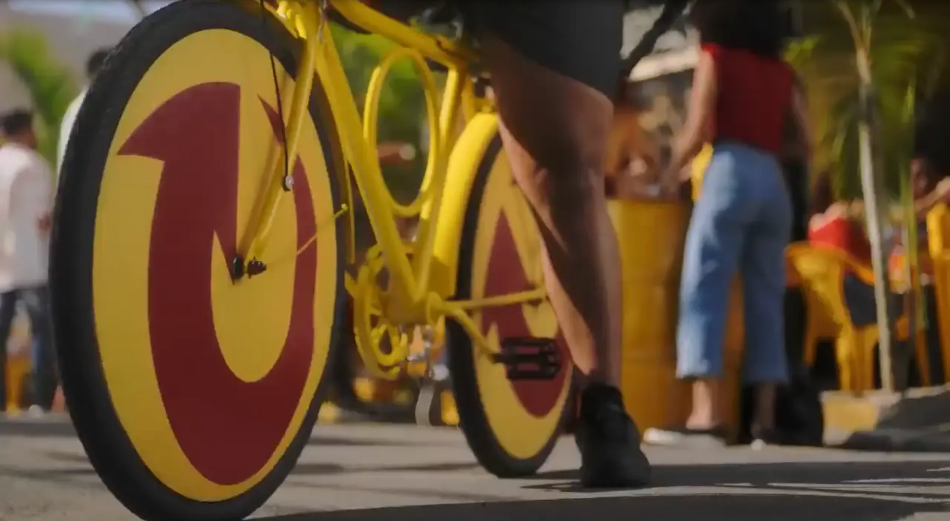 Uma pessoa está andando de bicicleta amarela com um círculo vermelho na roda dianteira.