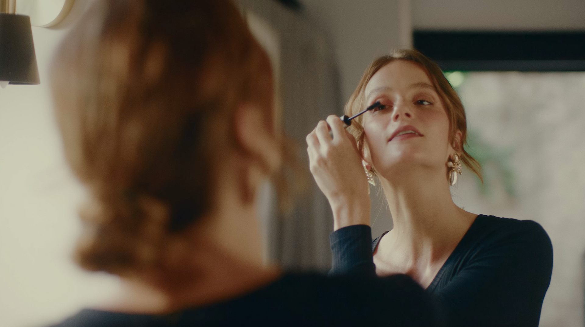 Uma mulher está aplicando rímel nos cílios em frente a um espelho.