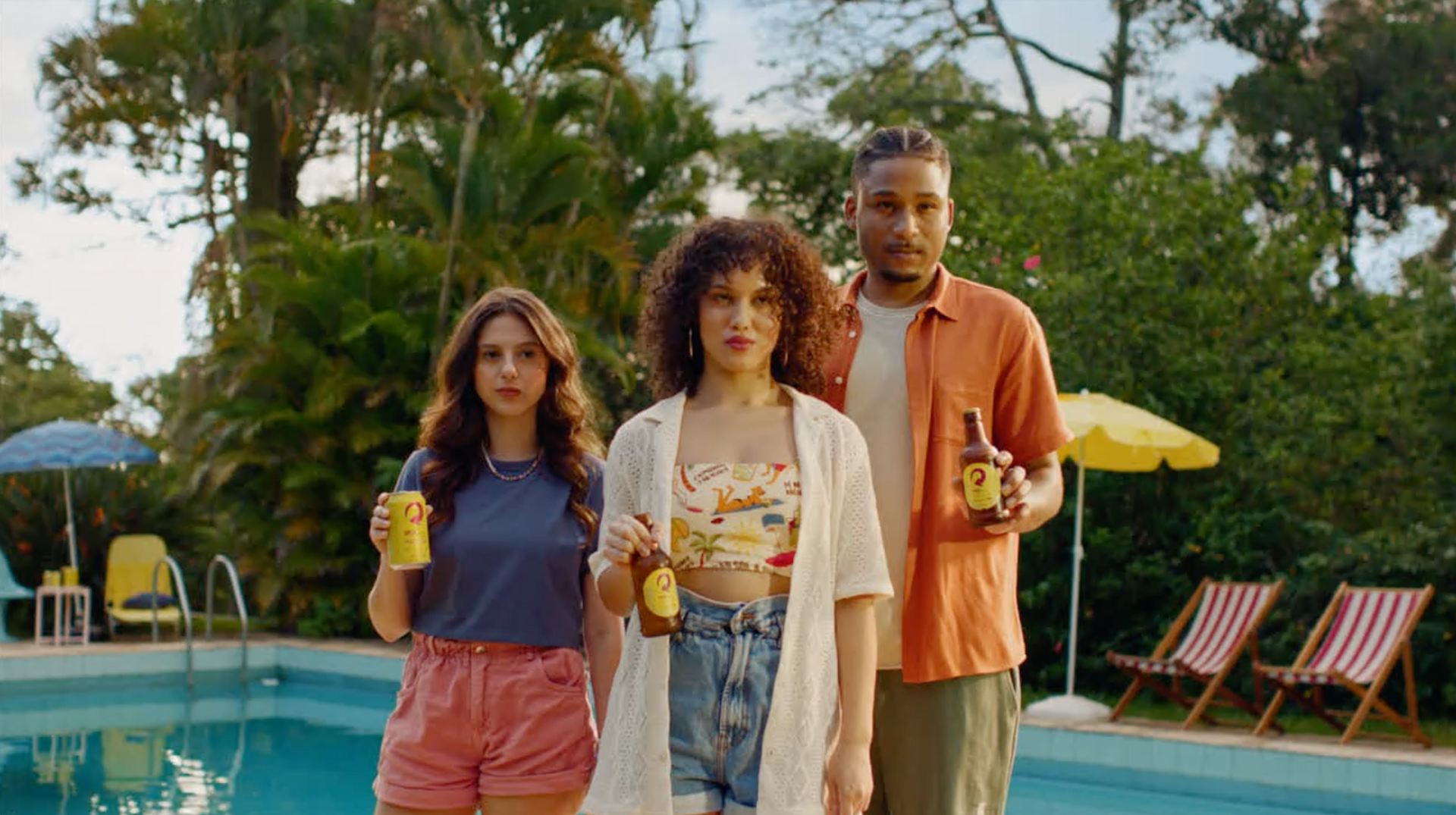 Um grupo de pessoas está parado ao lado de uma piscina segurando garrafas de cerveja.