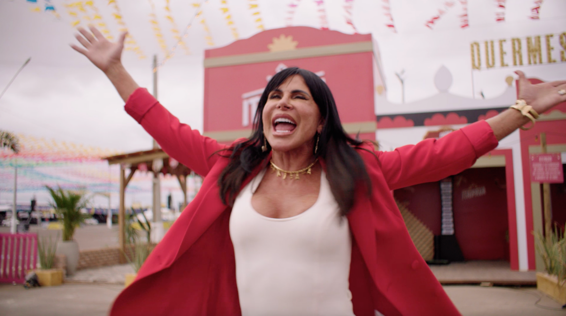 Uma mulher com uma jaqueta vermelha está parada em frente a um prédio vermelho com os braços estendidos.