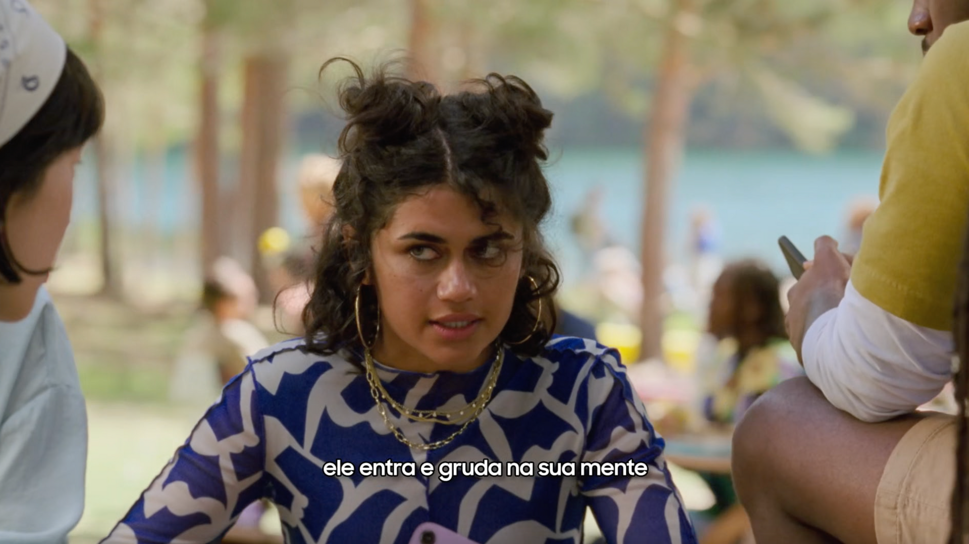 Uma mulher com um vestido azul e branco está sentada à mesa com outras pessoas.