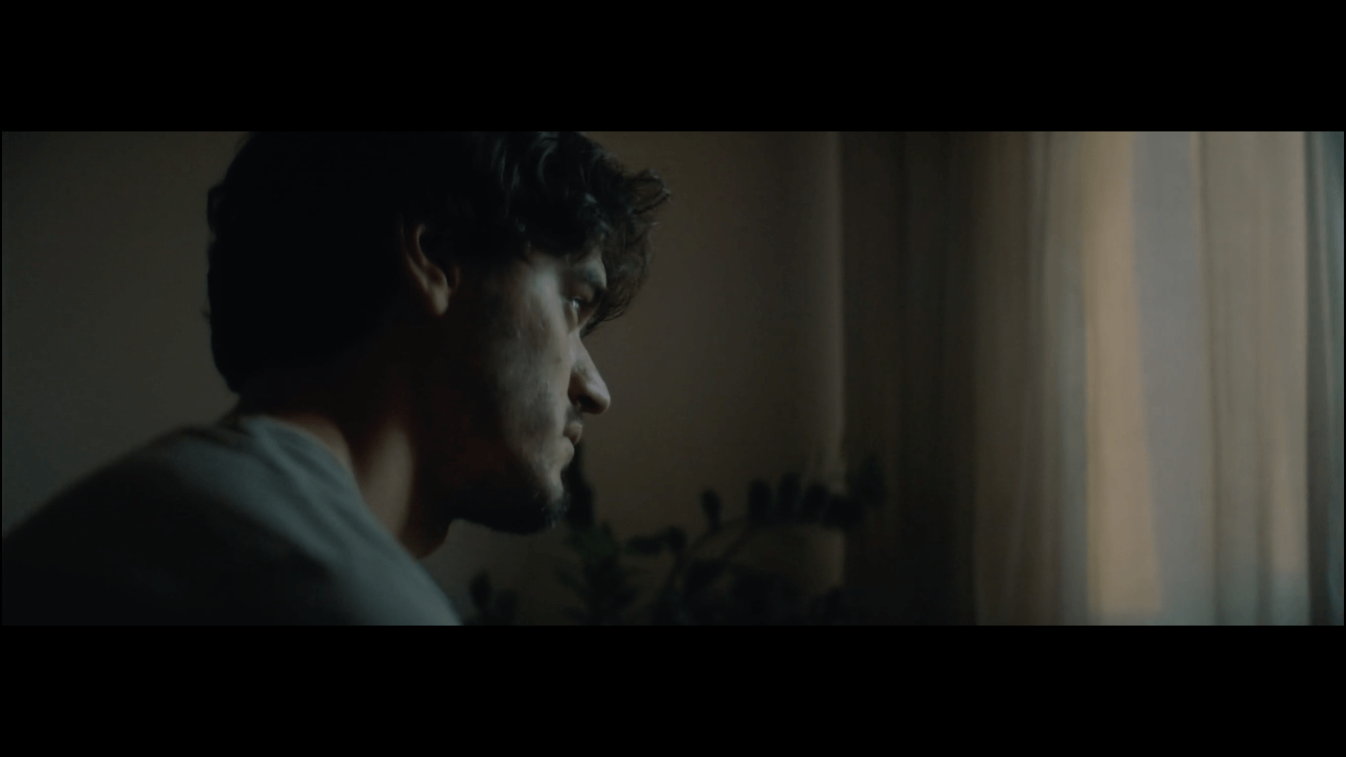 Um homem está olhando pela janela de um quarto escuro.