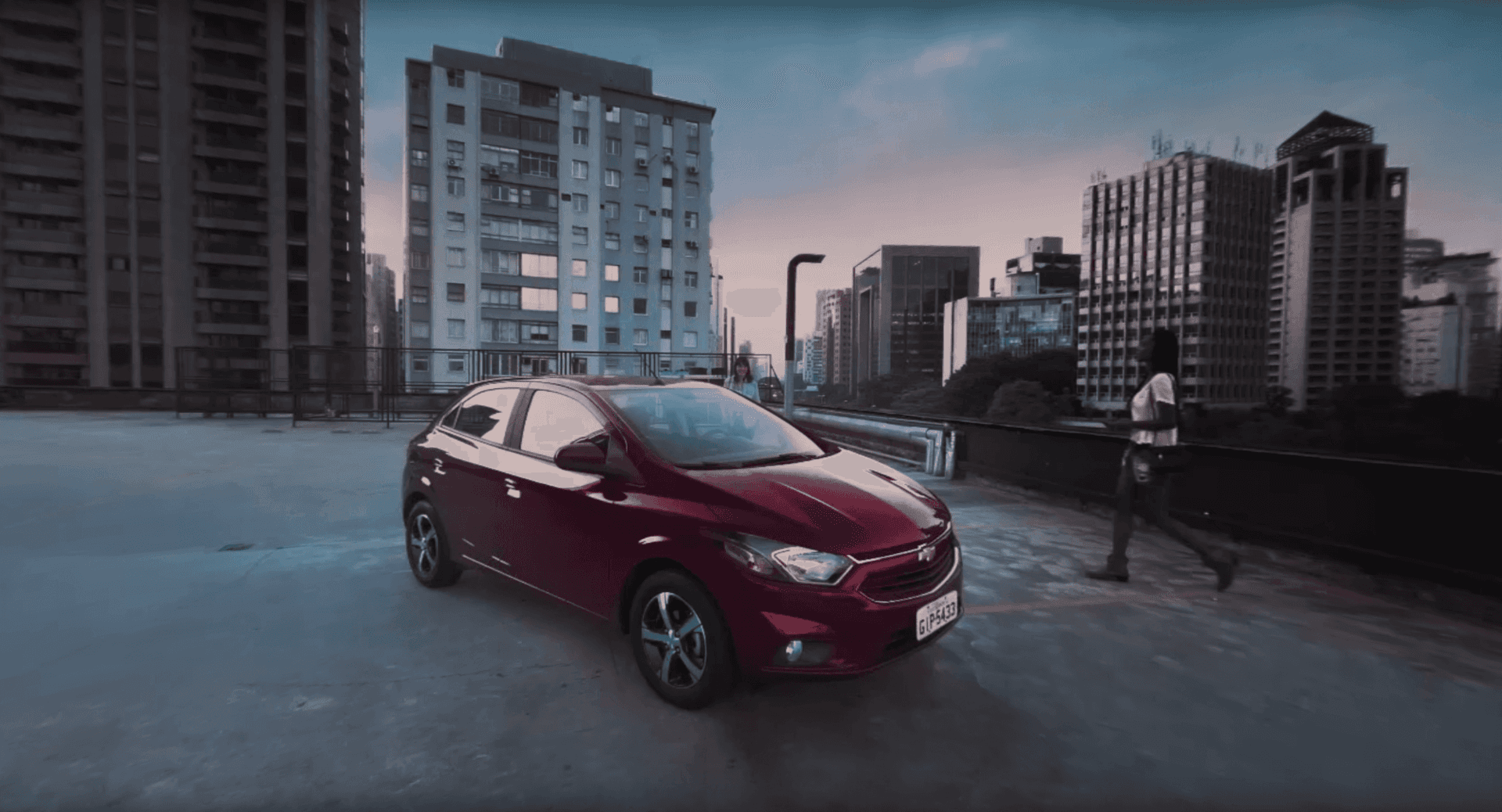 Um carro vermelho está estacionado em um estacionamento em frente a uma cidade.