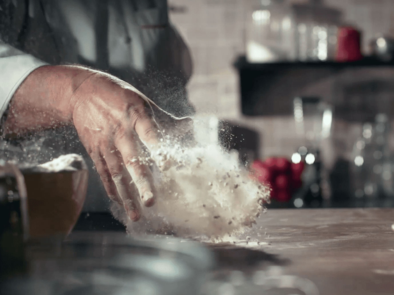 Uma pessoa está espalhando farinha sobre uma mesa de cozinha.