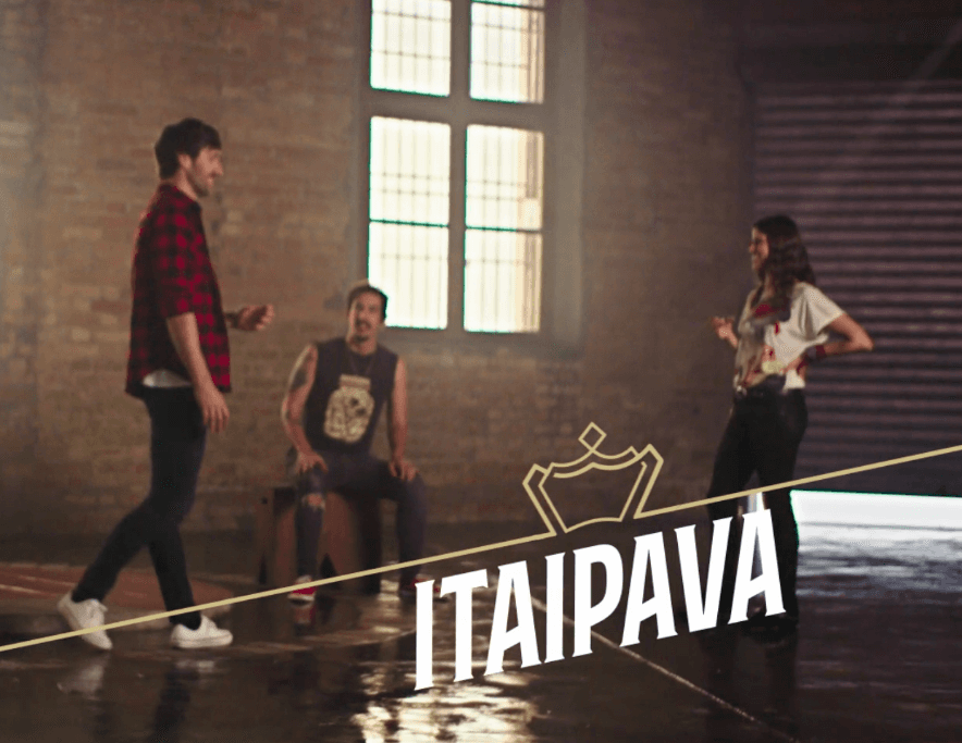 Um grupo de pessoas dança em uma sala com a palavra itaipava no chão.