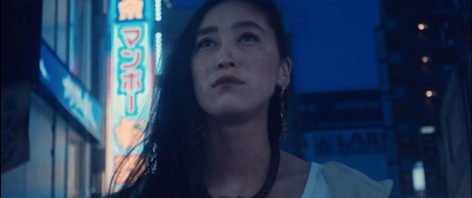 Uma mulher está parada em frente a um letreiro de néon à noite.