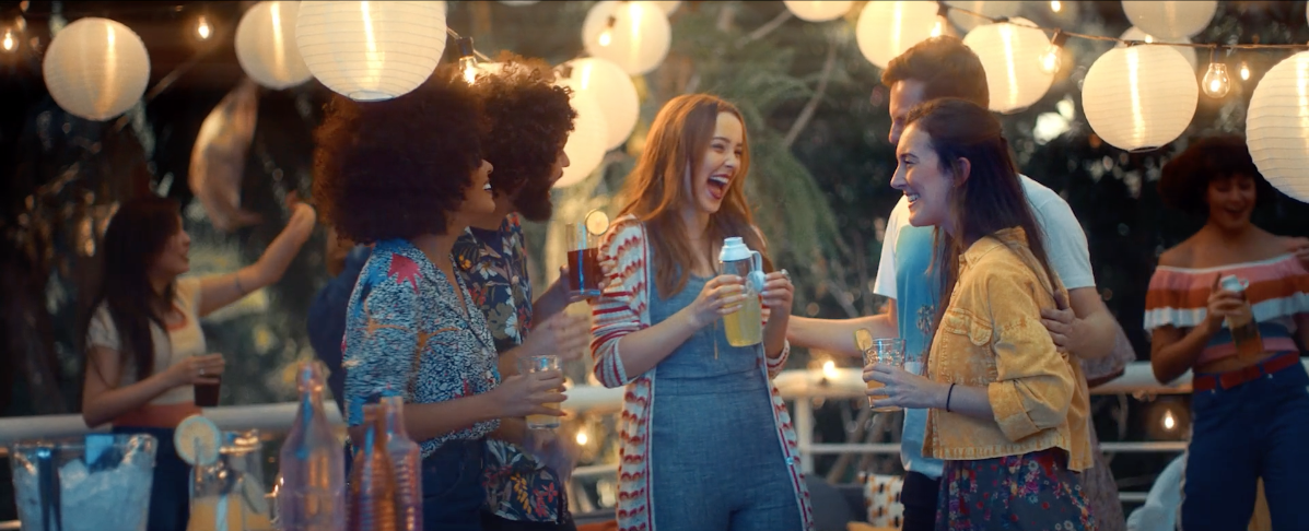 Um grupo de pessoas está em volta de uma mesa segurando bebidas em uma festa.