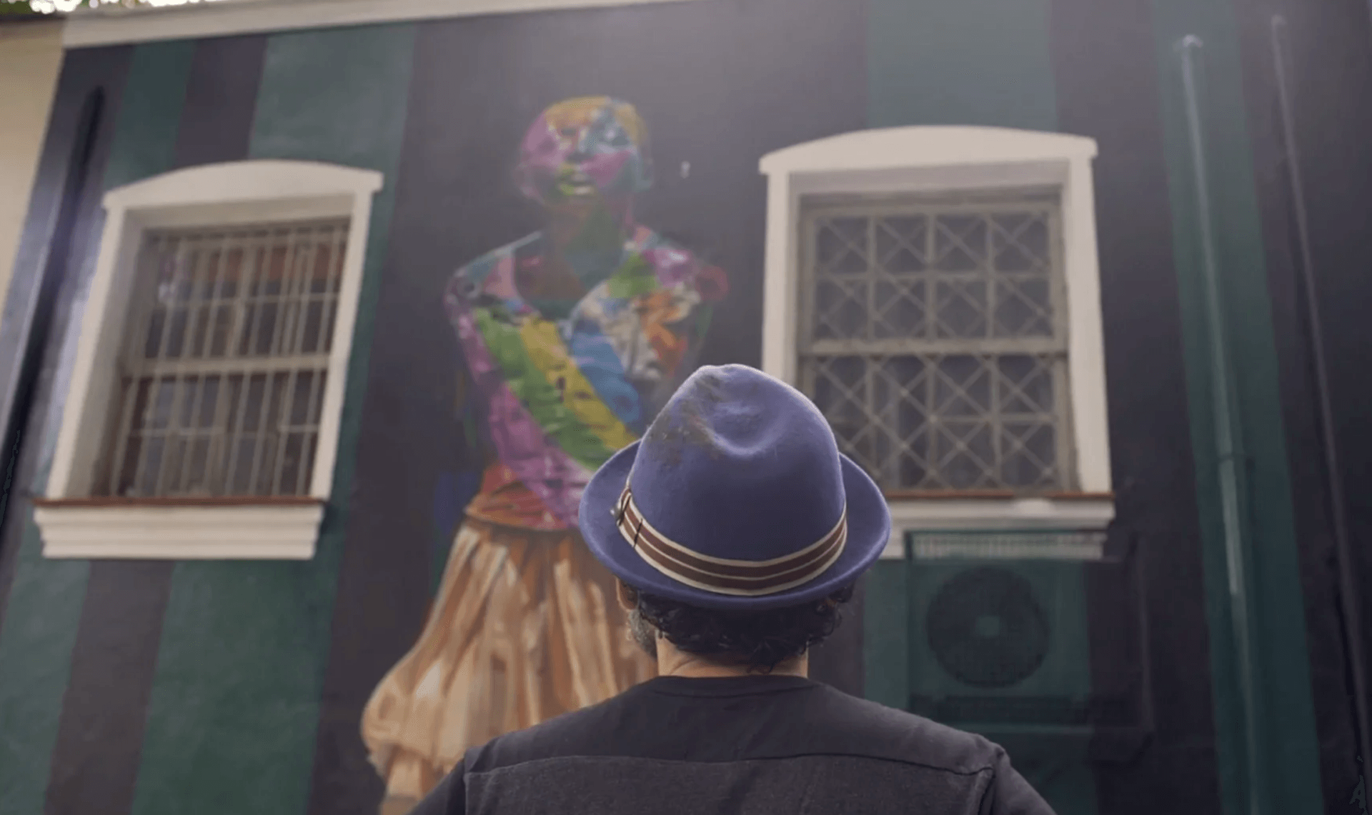 Um homem de chapéu está olhando para uma pintura na parede.