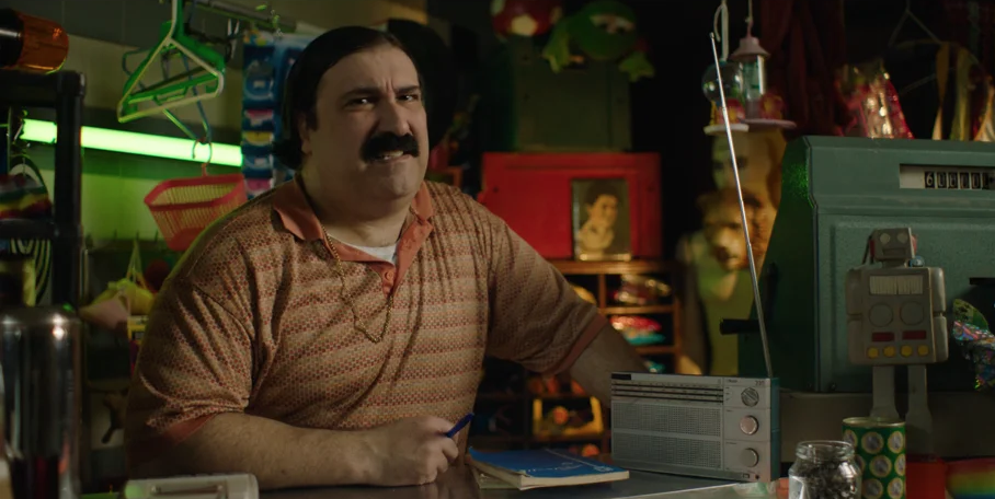 Um homem de bigode está sentado no balcão de uma loja.