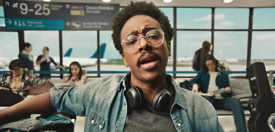 Um homem usando fones de ouvido e óculos está parado na sala de espera de um aeroporto.