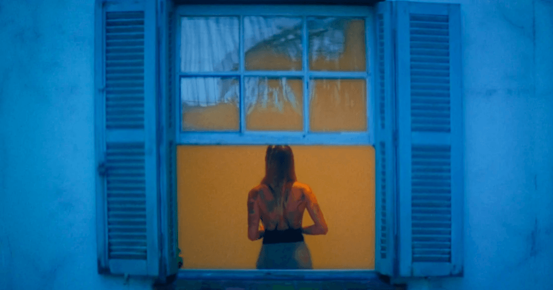 Uma mulher está diante de uma janela com venezianas azuis.