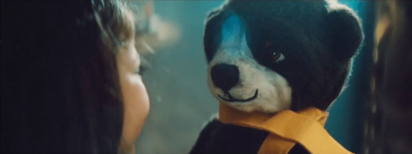 Uma menina está olhando para um bicho de pelúcia com um lenço no pescoço.