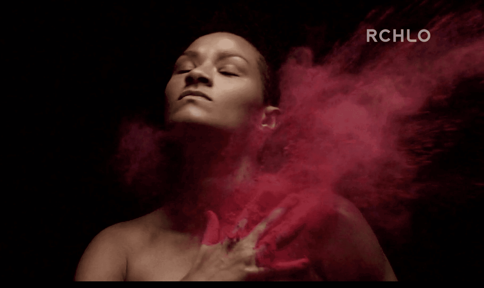 Uma mulher está cercada por um pó vermelho sobre um fundo preto.