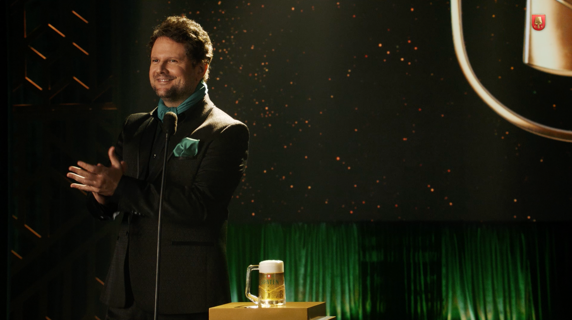 Um homem de terno está diante de um microfone em um palco.